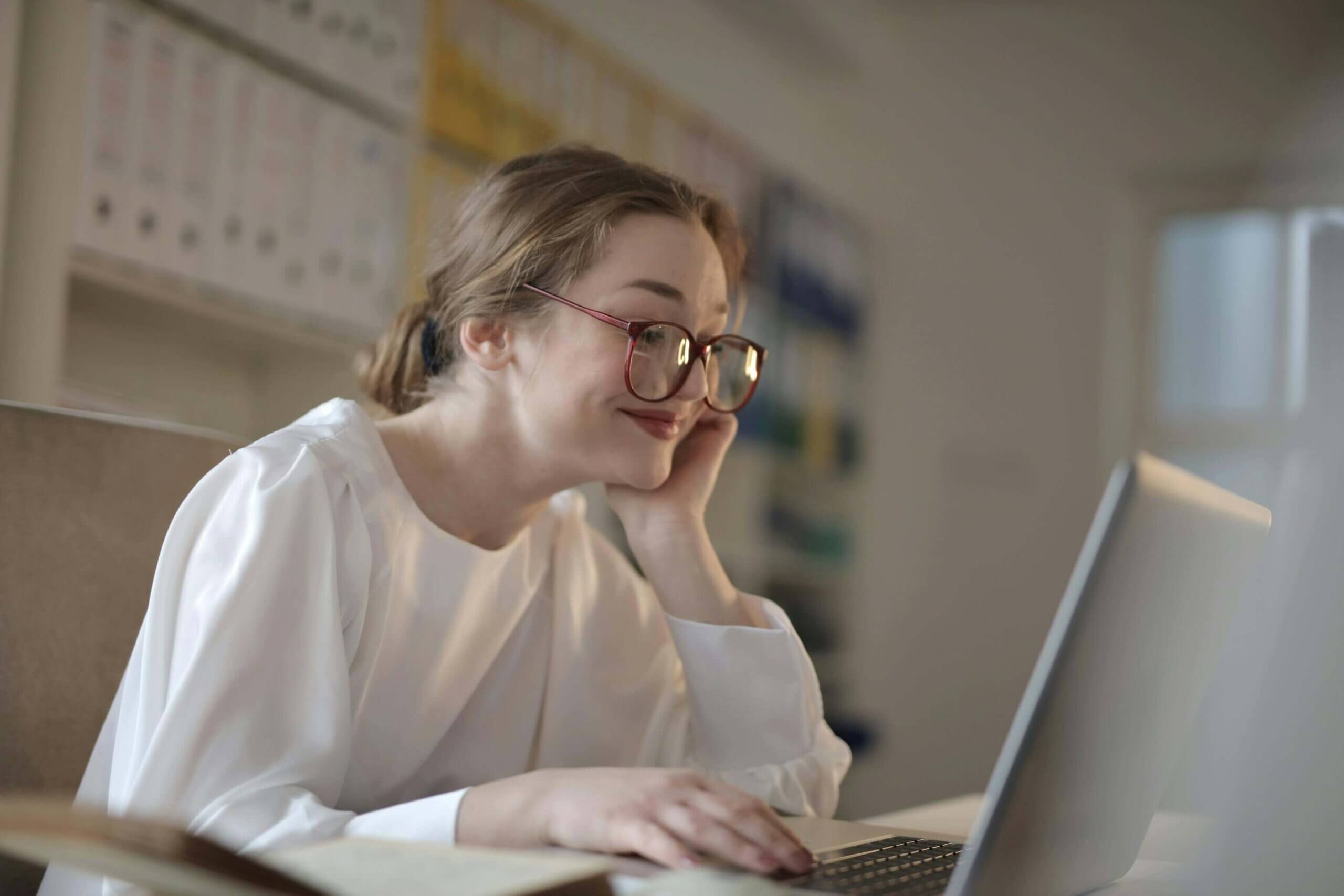 Woman in white long sleeves using a laptop for online ADHD therapy session.